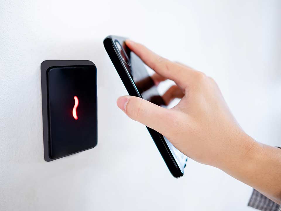 person holding a smartphone up to an access control box mounted on a wall